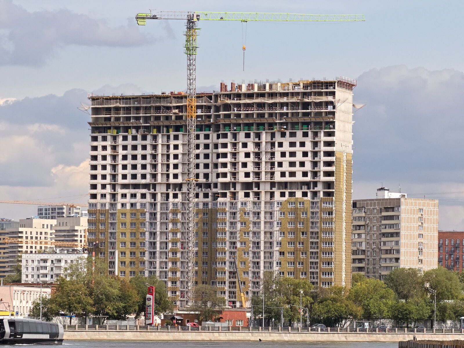 Edifício residencial em construção, com estrutura de concreto nos pavimentos de cima e fachada em acabamento nos de baixo, e uma grua ao lado.